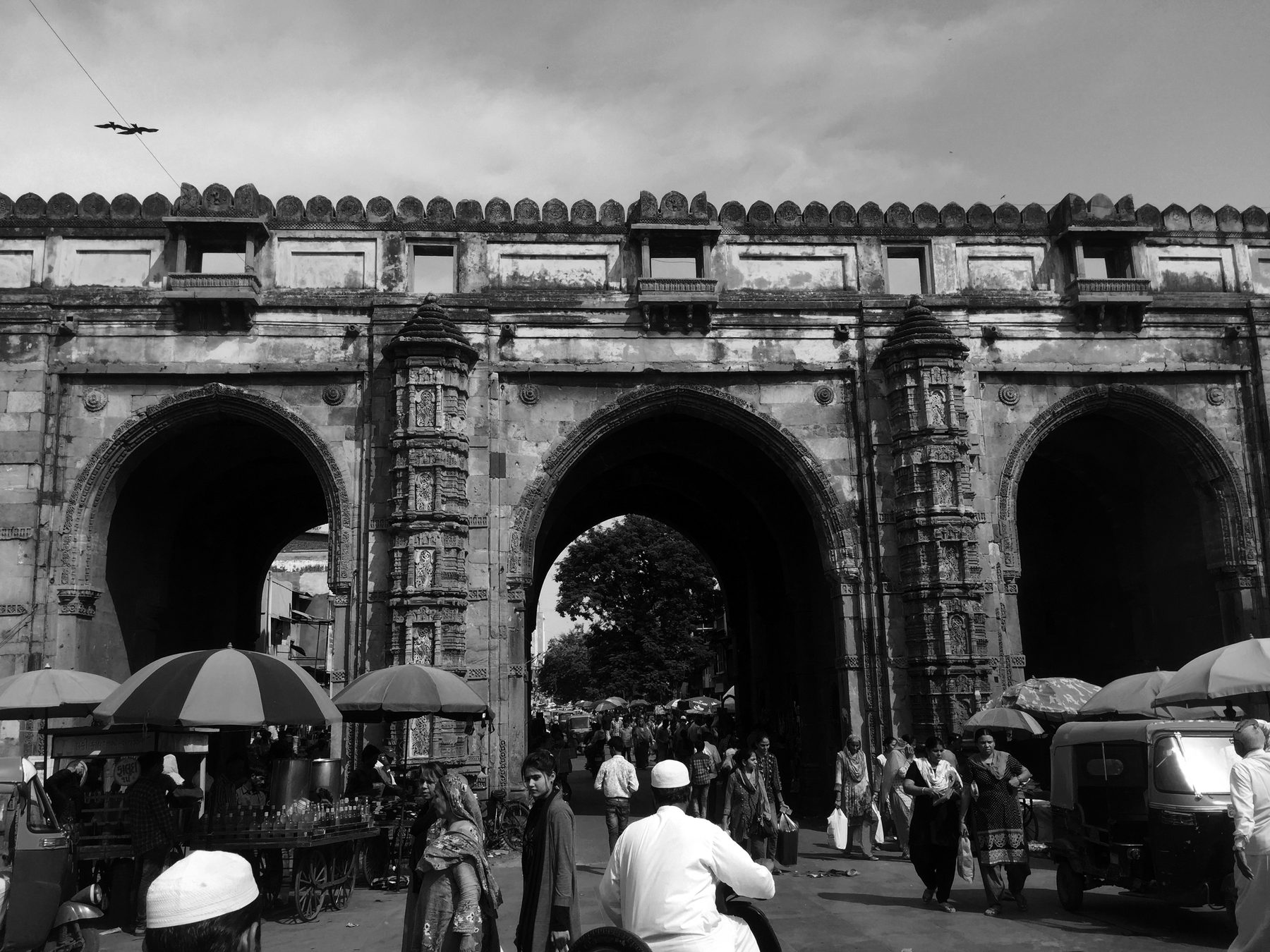 Teen Darwaza. Vendors and umbrellas at the foot of the gate, the only way up hidden behind them.