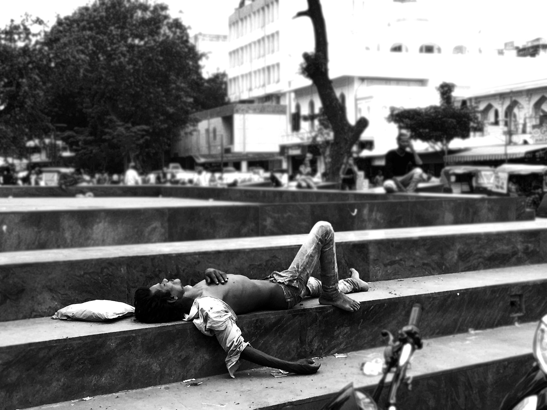Asleep on the steps. The plaza's edges and benches are someone's home at every hour of the day.