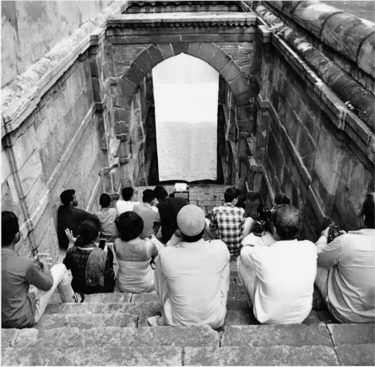 Eight in the evening. The steps of the vav as seating, the screen in the arch below, the audience facing the well.